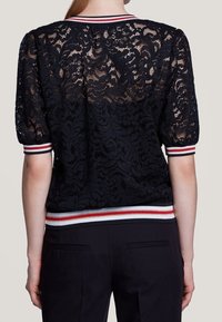 Schwarzes Spitzenoberteil mit puffärmel, Rundhalsausschnitt und rot-weißen gestreiften Rippbündchen und Saum. Durchscheinende Textur und Blumenmuster.