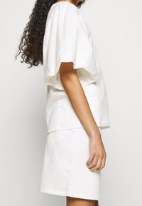 Blusa de algodón blanca con mangas abullonadas, combinada con una falda de mezclilla blanca. El conjunto presenta un corte relajado y un diseño minimalista.