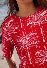 Rotes Kurzarmhemd mit einem weißen Palmenblättermuster, Rundhalsausschnitt und strukturiertem Stoff.