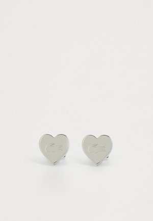 Pendientes en forma de corazón de metal plateado con una superficie pulida y un sutil detalle de logo grabado. Diseño simple y moderno, adecuado para el uso diario.