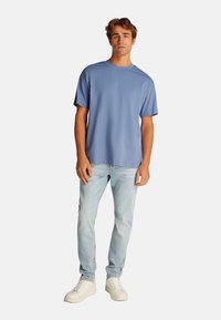 Camiseta de algodón azul claro con cuello redondo y mangas cortas, combinada con jeans de mezclilla de lavado claro y zapatillas blancas. Diseño simple y casual.