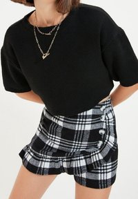 Maglione nero cropped a maniche corte, abbinato a una minigonna a quadri bianco e nero con bottoni in argento e orlo arricciato.