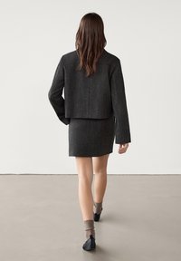 Gray textured cropped jacket paired with a matching mini skirt, viewed from behind. Model wears black flats and brown ribbed socks.