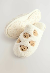 White fuzzy slippers with bear face accents, soft texture, and a cushioned sole featuring a star and moon pattern.