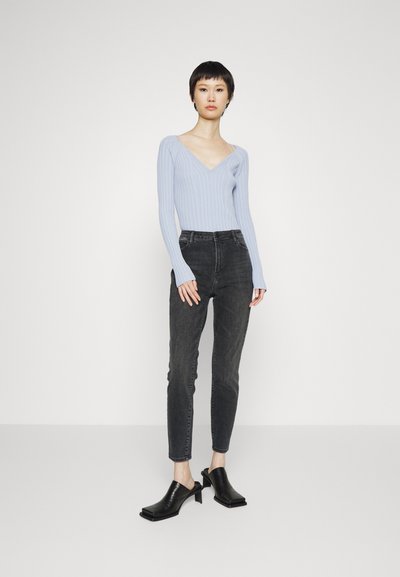 Suéter azul claro com nervuras e decote em V, combinado com jeans slim-fit cinza escuro e mules pretas abertas, com biqueira quadrada e saltos robustos.