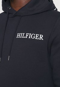 Sudadera navy de mezcla de algodón, con el logo blanco 'HILFIGER'. Incluye cordón ajustable y tela de textura fina.