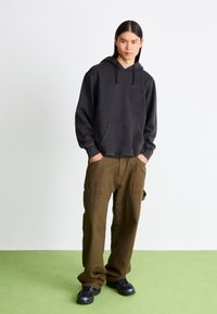 Black hoodie with front pocket and drawstrings paired with loose olive cargo pants. Worn with chunky black sneakers on green background.