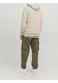 Beige hoodie, olijfgroene cargobroek met zijzakken en witte sneakers. Eenvoudig ontwerp, katoenen stof, relaxed fit.