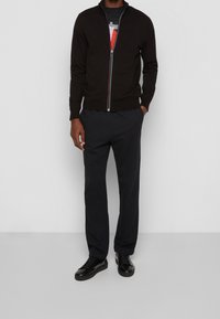 Svart zip-up tröja med färgglada dragkedjedetaljer, i kombination med svarta byxor och svarta sneakers. Slät textur, skräddarsydd design.