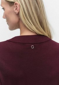 Bordowy sweter dziany z okrągłą srebrną aplikacją na plecach, prezentujący prążkowaną teksturę oraz klasyczny fason kołnierzyka.