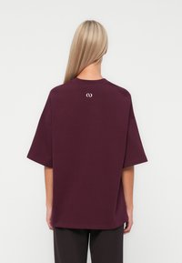 Burgundy oversized t-shirt made of cotton features a crew neckline, short sleeves, and a subtle logo on the upper back.
