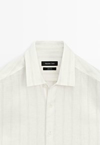 White linen button-up shirt with subtle vertical stripes and a classic collar, labeled Massimo Dutti, made in China.