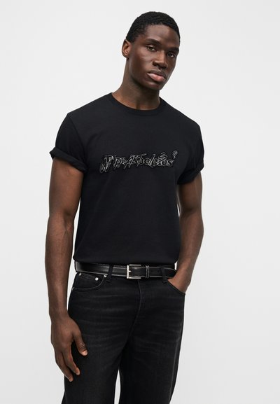 Μαύρο βαμβακερό t-shirt με γυρισμένα μανίκια, διακοσμημένο με γραφικό σχέδιο σε ασημί κλωστή. Συνδυασμένο με μαύρο τζιν και μαύρη ζώνη.