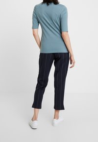 Camiseta de manga corta, de color azul claro, hecha de tela suave, combinada con pantalones oscuros con rayas blancas verticales y zapatillas blancas.
