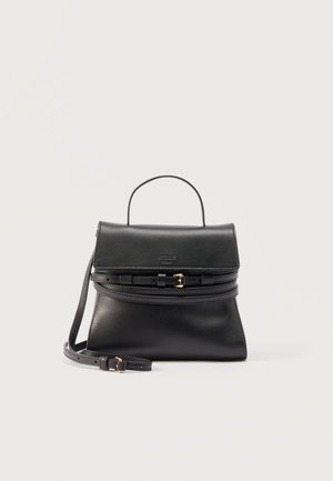 Sac à main en cuir noir avec poignée supérieure, fermeture à rabat, doubles sangles à boucle et bandoulière amovible sur un fond neutre.