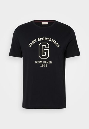 Tengerészeti pamut póló kerek nyakkivágással és rövid ujjakkal. Fehér felirattal rendelkezik, amely a következőket tartalmazza: "GANT SPORTSWEAR," "NEW HAVEN," és "1949."