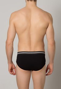 Slip da uomo neri con una vita a righe grigie, realizzati in tessuto morbido, progettati con una vestibilità aderente e un taglio arrotondato per garantire comfort.