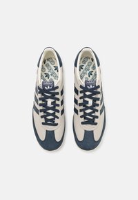 Adidas Sneaker mit einem hellbraunen Leder-Obermaterial und marineblauen Wildlederakzenten, drei marineblauen Streifen und einer gemusterten Innensohle.