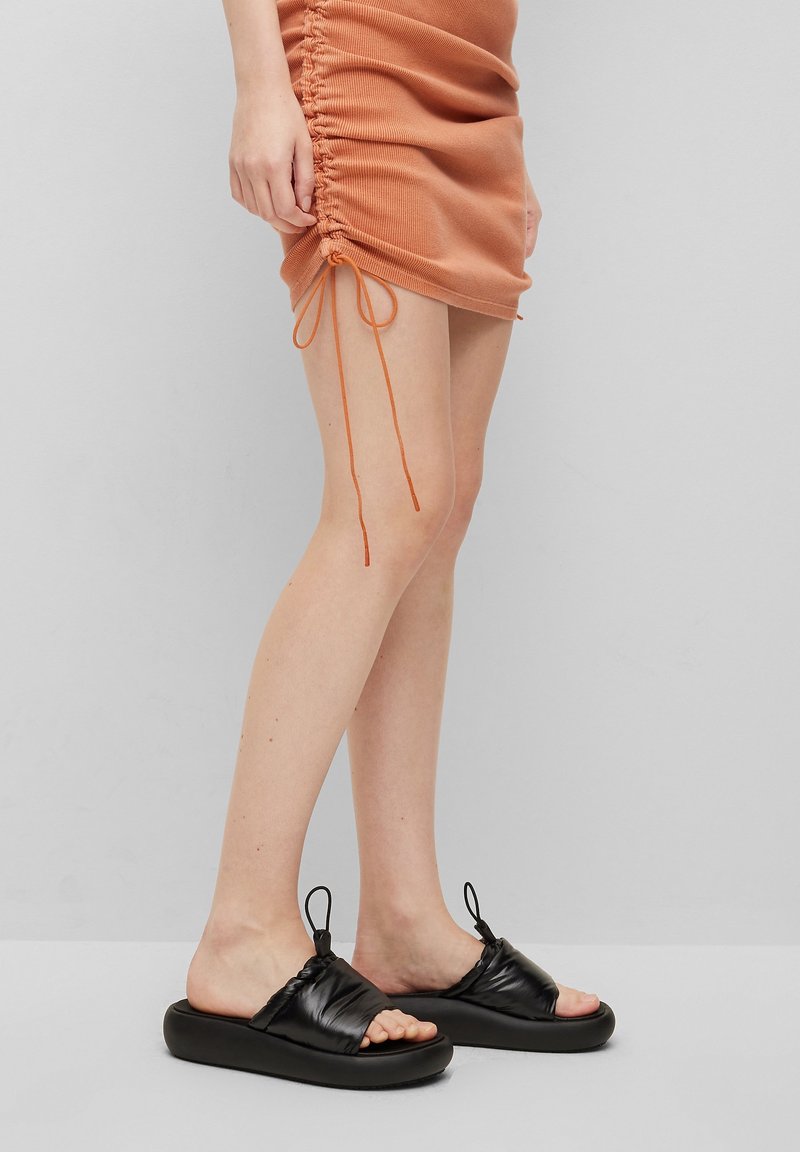 Czarne klapki z miękką, marszczoną cholewką i grubą podeszwą. Widzoczne detale teksturowane oraz mała pętelka z tyłu dla łatwego zakładania.