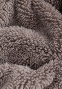 Gros plan sur un tissu doux et duveteux de couleur taupe avec une surface en polaire épaisse, texturée et confortable.