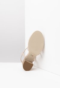 Sandalo beige con tacco alto, dotato di fasce sottili e suola texturizzata. Presenta una punta rotonda e una soletta con marchio. Design minimalista.