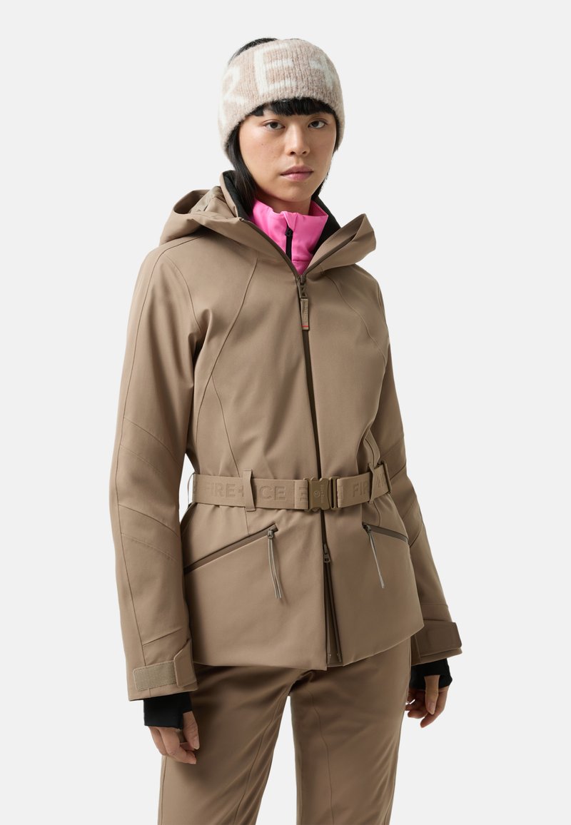 Braune wasserfeste Jacke mit Kapuze, mit tailliertem Schnitt, Reißverschlusstaschen und schwarzen Bündchen. Über einem pinken Oberteil getragen.