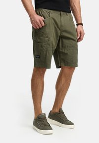 Shorts cargo olive avec une coupe décontractée, plusieurs poches et un tissu texturé. Conception légère adaptée à une tenue décontractée.