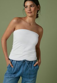 Haut blanc sans manches avec une coupe ajustée, en coton doux. Assorti à un pantalon en denim bleu clair avec cordon de serrage et poches latérales.