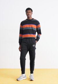 Fekete, hosszú ujjas póló, színes vízszintes csíkokkal, fekete cargo nadrággal párosítva, oldalzsebekkel és logóval. Ezüst sportcipők.