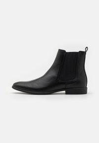 Zwarte leren enkelboots met elastische zijpanelen, een taps toelopende neus en een lage blokhak. Gladde textuur met een aantreklipje aan de achterkant.
