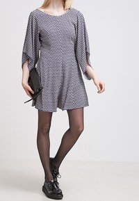 Šaty s krátkým rukávem, vzorované v námořnické modři a bílé, mírně rozšířeného střihu s bočními kapsami. Nosí se s černými punčochami a platformovými botami.