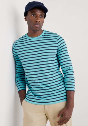 Long-sleeve striped t-shirt in turquoise and navy, cotton material, crew neck, soft texture, worn with light beige pants.