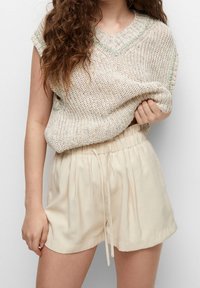 Knit beige short-sleeve top with green accents, paired with light beige drawstring shorts. The top features a loose, textured design.