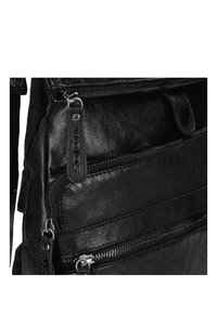Zaino in pelle nera con più scomparti con zip, superficie testurizzata e un'etichetta in pelle con il marchio. Presenta dettagli in metallo argentato.