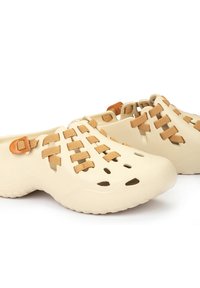 Zuecos beige con un cuerpo de goma texturizada, correas de tela trenzada y un hebilla lateral. Cuenta con orificios de ventilación para mayor transpirabilidad.