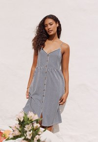 Robe d'été rayée aux couleurs bleu marine et blanc, corsage ajusté avec fermeture boutonnée sur le devant, fines bretelles et jupe évasée avec une fente latérale.