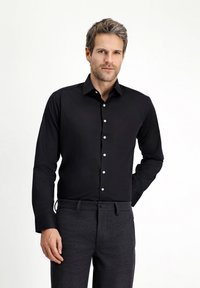 Czarna koszula na długi rękaw z guzikami, z zaostrzonym ko�łnierzykiem i białymi guzikami, zestawiona z ciemnoszarymi spodniami. Gładka tkanina, dopasowany krój.