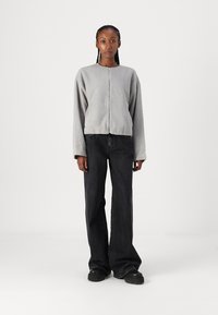 Grå fleece zip-up jakke med en kort design, avslappet passform og lange ermer, kombinert med svarte vide jeans og store svarte sko.