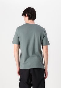 Camiseta de manga corta en verde suave, hecha de material de algodón suave, que muestra un diseño de cuello redondo simple. Vista desde la parte de atrás.