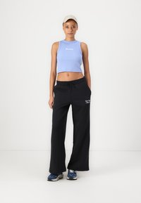 Lys blå cropped tank top med hvit logo, sammen med svarte vide joggebukser med hvit tekst. Fullført med en beige caps og blå sneakers.