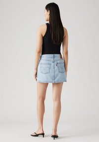 Lyseblå denim skjørt med frynset kant, to baklommer og en brun lærlabel. Kombinert med en svart ermeløs topp og sorte sandaler.