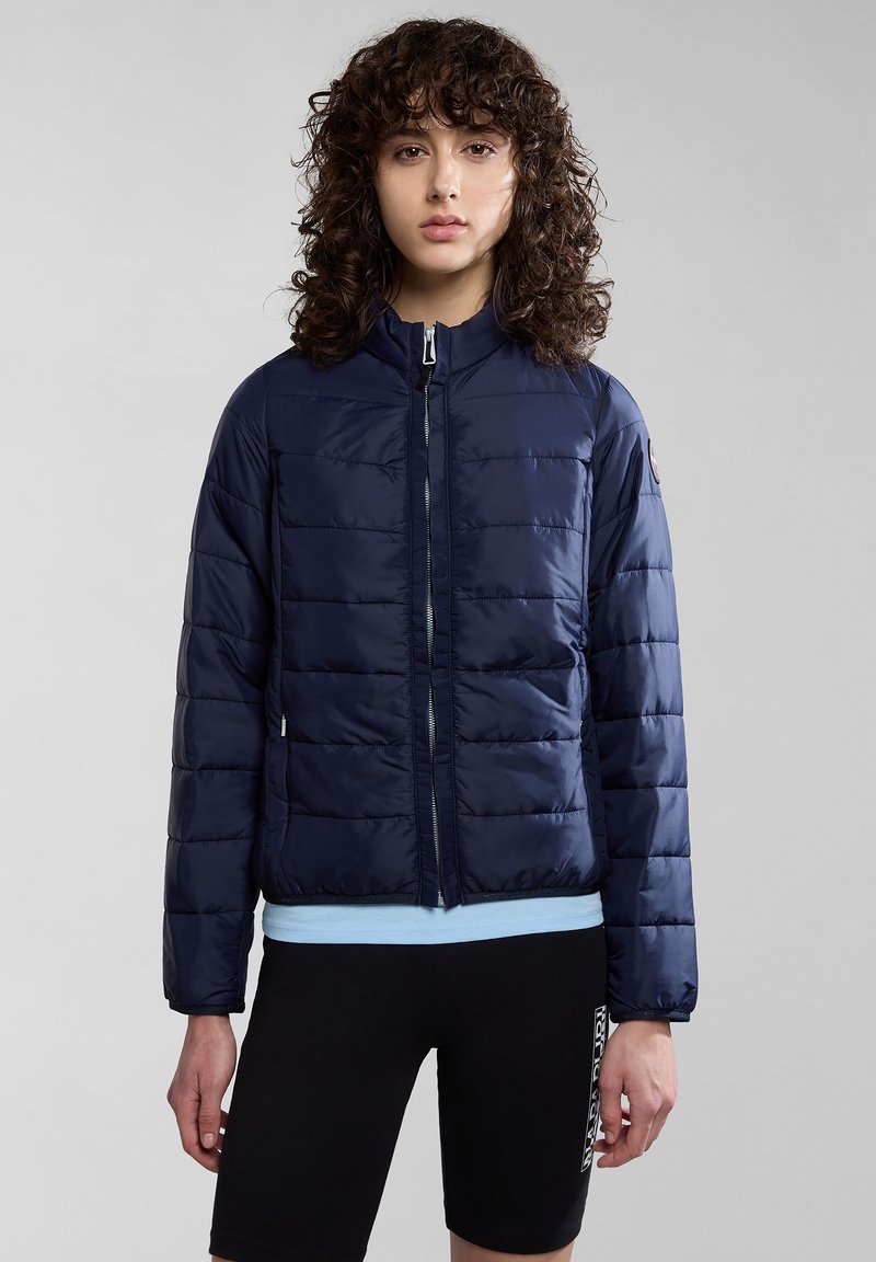 Mörkblå vadderad pufferjacka med hög krage, framdragkedja och sidofickor. Smala horisontella sektioner skapar en slank textur.