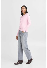 Helle pinke Langarm-Strickjacke aus weichem Stoff, kombiniert mit hellgrauen, weit geschnittenen Jeans und dunkelbraunen Knöchelstiefeln.