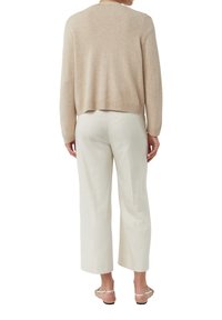 Beżowy sweter z dzianiny z prążkowanym dołem, noszony na białych szerokich spodniach. Posiada długie rękawy i luźny krój.