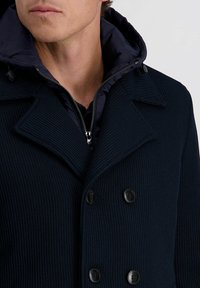 Dunkelblaue gerippte Jacke mit doppelreihiger Knopfverschluss, großem Kragen und abnehmbarer gesteppter Kapuze. Glatte Textur und strukturiertes Design.