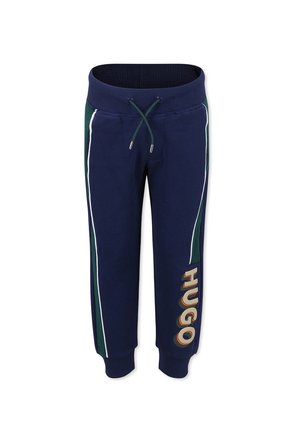 Pantalons de survêtement bleu marine en matériau doux, présentant des bandes latérales blanches et un accent vert, avec un grand logo "HUGO" sur la jambe gauche.