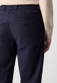 Pantalone od pamučne mješavine tamnoplave boje s glatkom teksturom, s potnjim džepom i oznakom Calvin Klein, nosi se s laganom majicom.