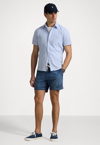 Chemise à manches courtes rayée bleu et blanc, short en denim, casquette marine et baskets décontractées. Comprend une poche et un short à cordon.