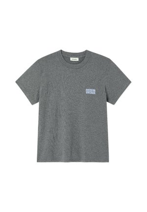 Personne debout portant un t-shirt gris à manches courtes, un jean large bleu clair et des chaussures noires sur un fond blanc uni.