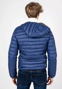 Giacca a vento blu con un design trapuntato e cappuccio, caratterizzata da una texture liscia e un accento di tessuto a contrasto sulle spalle.